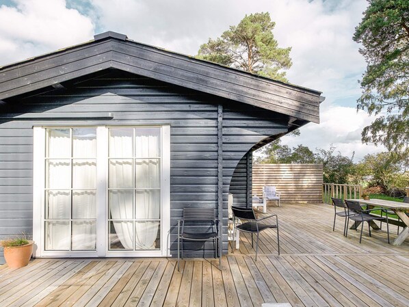 A cabin with a large sliding glass door, a deck with outdoor furniture, and a sloped roof.