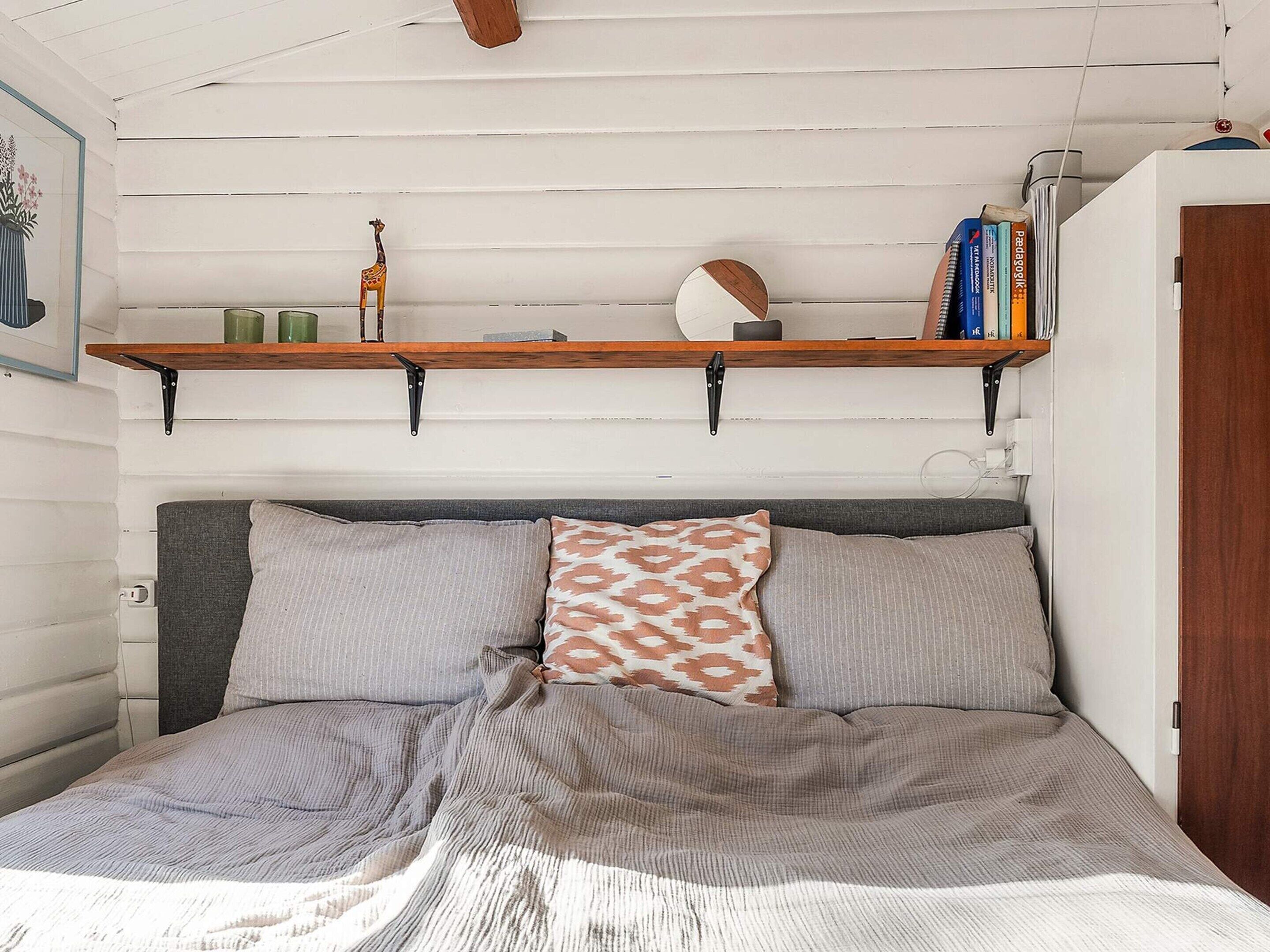 Ein Schlafzimmer mit einem Bett, Kissen, einem Regal mit Büchern und Dekoration sowie einem gerahmten Bild an der Wand.
