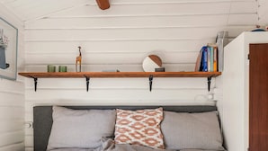 Quarto com cama, almofadas, estante com livros e objetos decorativos, e um quadro na parede.