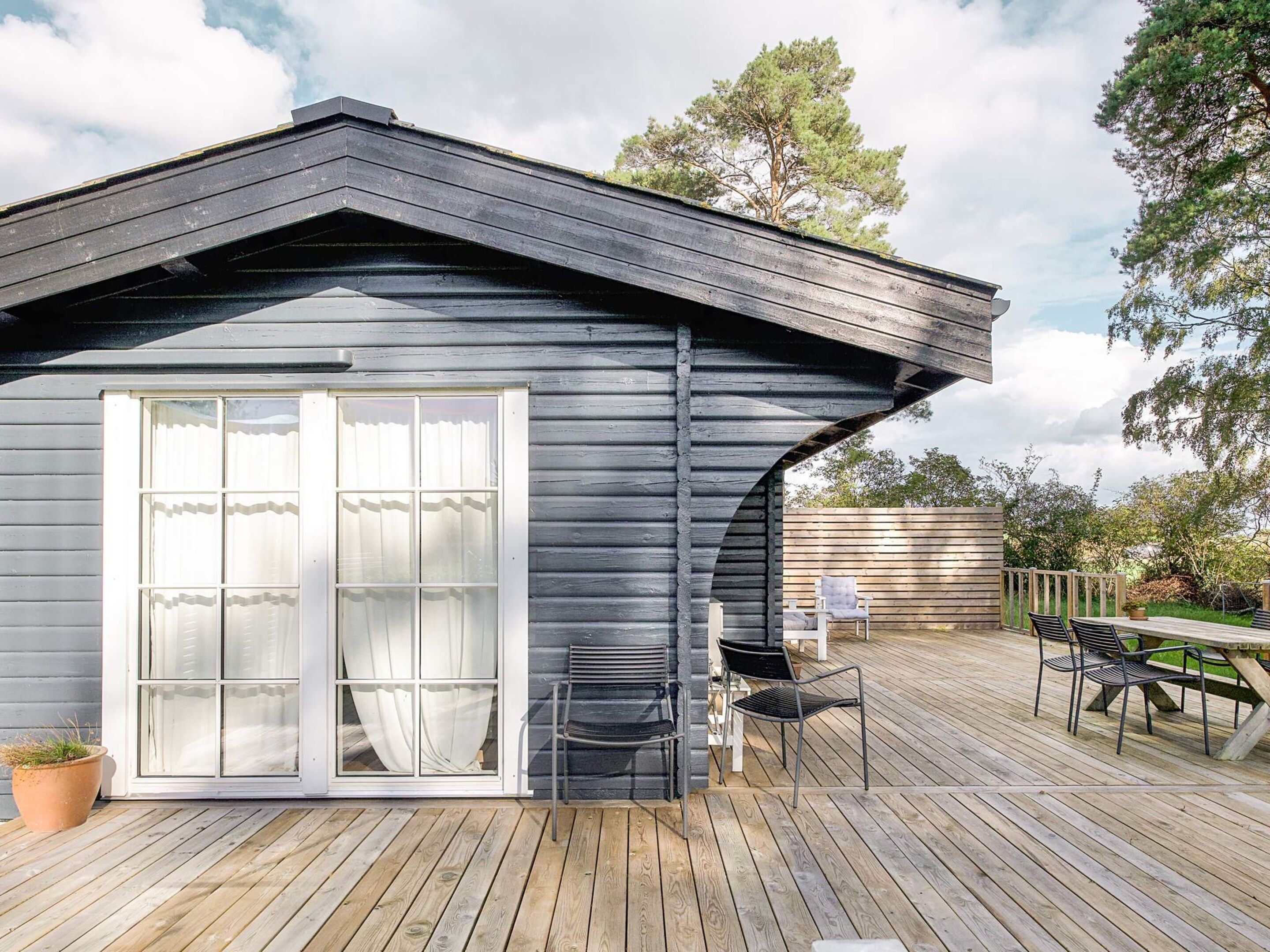 Eine Holzhütte mit einer großen Schiebeglasdoor, einer Terrasse mit Sitzgelegenheit und einem geneigten Dach.