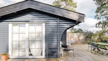 Eine Holzhütte mit einer großen Schiebeglasdoor, einer Terrasse mit Sitzgelegenheit und einem geneigten Dach.