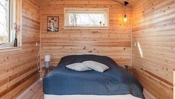 Een knus slaapkamer met een bed, nachtkastje, lamp en een raam.