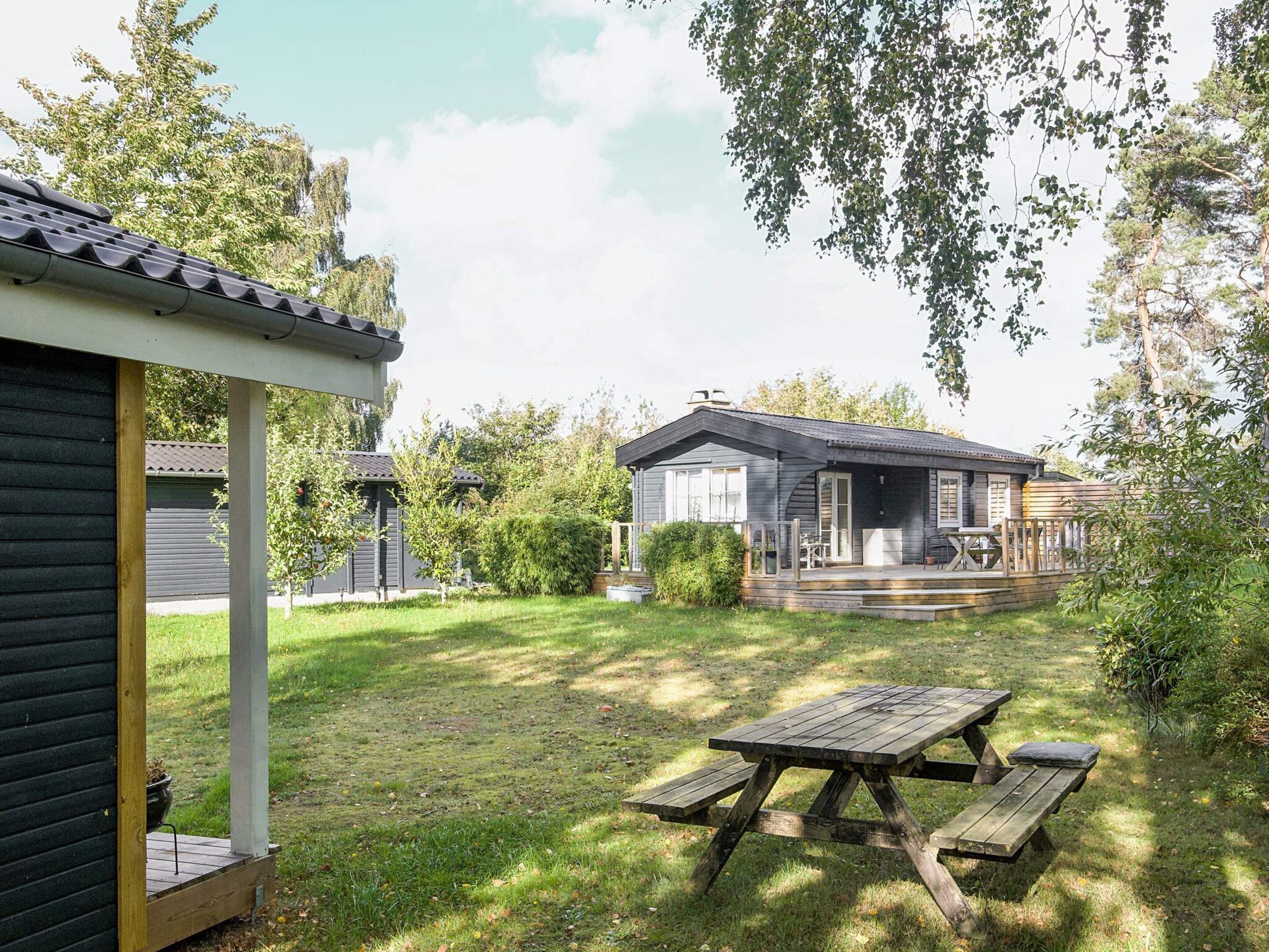 A wooden house with a porch and a picnic table in the yard.