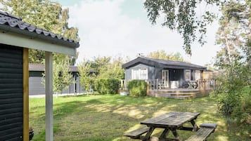 A wooden house with a porch and a picnic table in the yard.