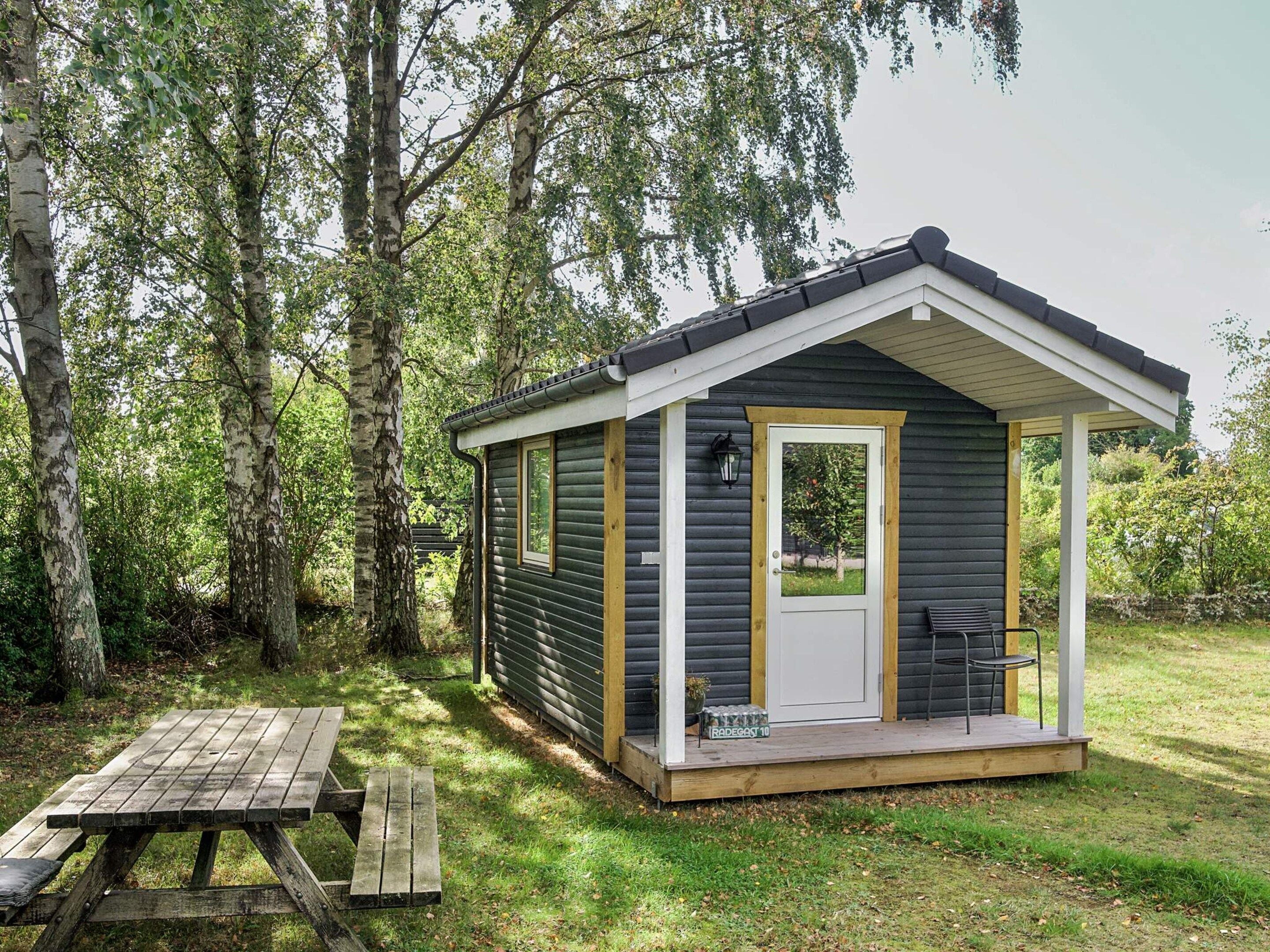 A small cabin with a porch, a picnic table, and a view of the surrounding forest.