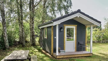 A small cabin with a porch, a picnic table, and a view of the surrounding forest.