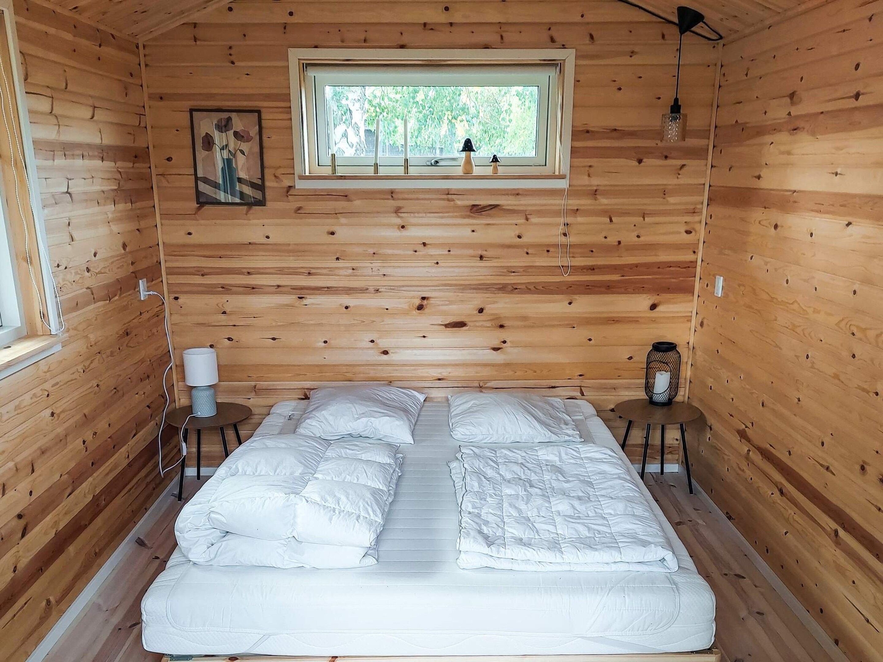 A wooden cabin room with a bed, a window, a lamp, and a small table.