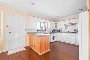 A modern kitchen with white cabinetry, a wooden island, and a built-in washer and dryer. - Spacious 4BR/4BA Vancouver Retreat | Near Downtown & UBC (Vancouver)