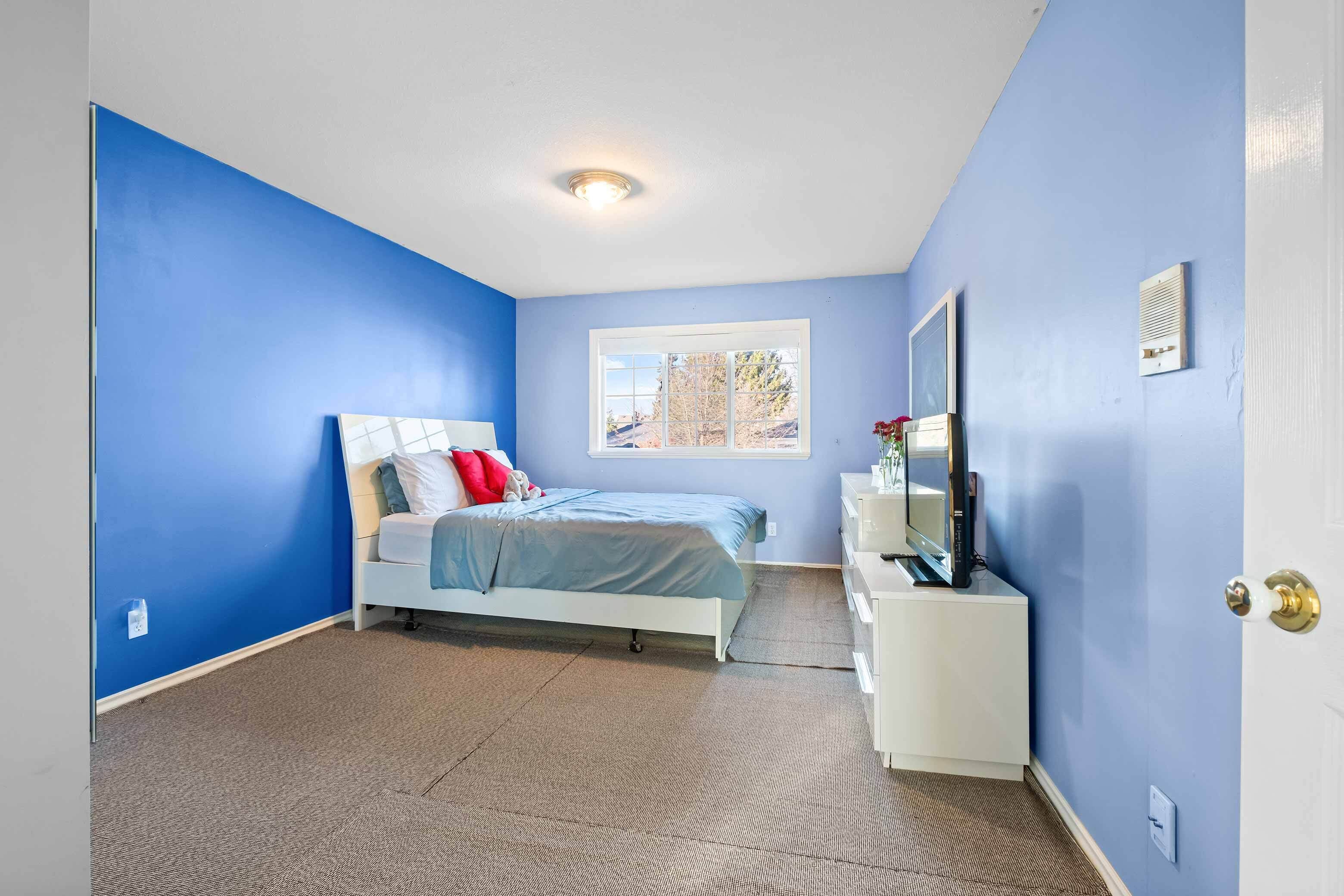 A bedroom with a bed, a window, a desk with a computer, and a door with a handle.