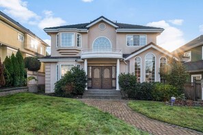A two-story house with a central entrance, a covered porch, and a brick pathway leading to the front door. - Spacious 4BR/4BA Vancouver Retreat | Near Downtown & UBC (Vancouver)
