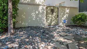 A paved pathway with stepping stones leading to a wooden gate, surrounded by a gravel area and greenery. - Ritz del Rio by Avantstay Single-level + BBQ Patio + Outdoor TV Quiet Cul-de-sac (Paso Robles)