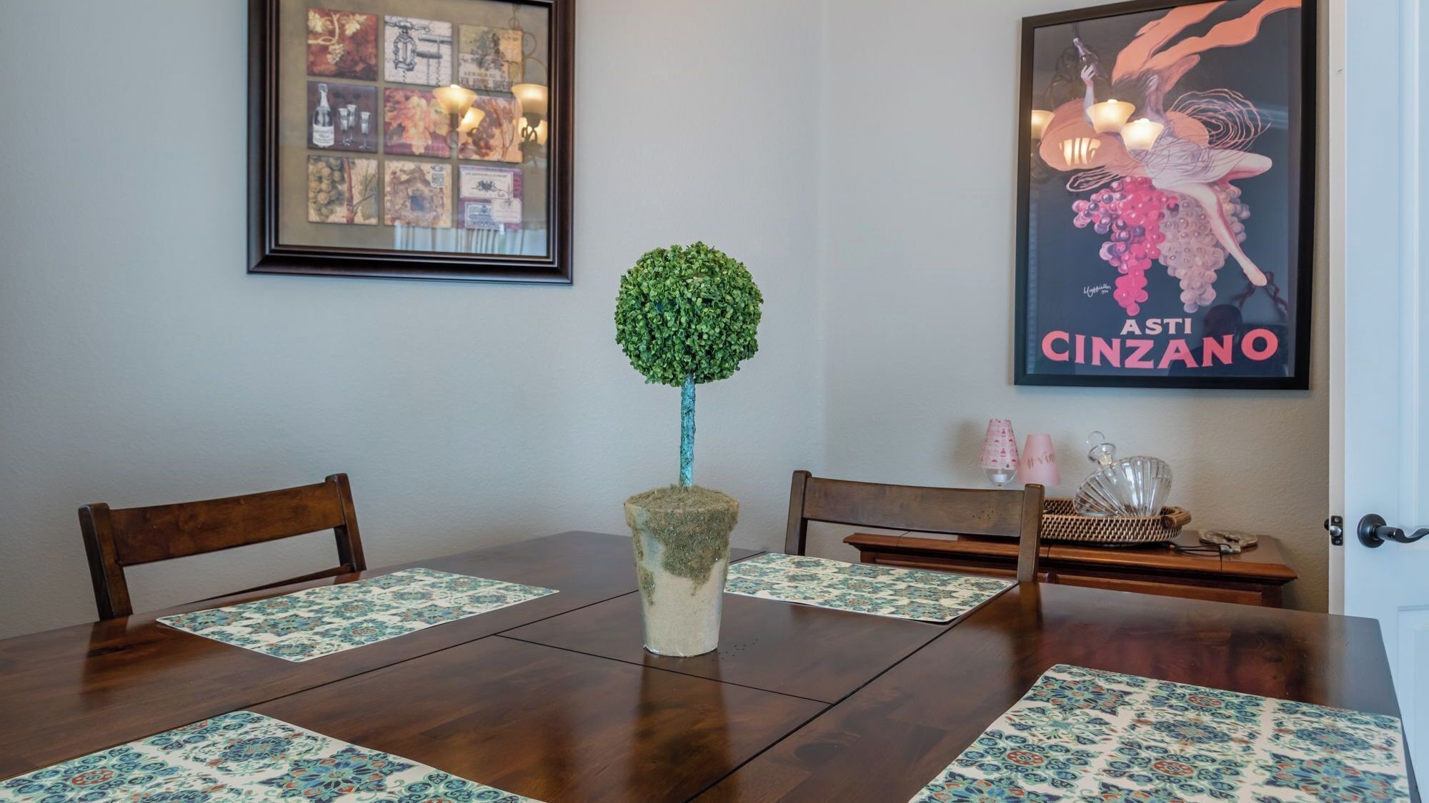 Een eetgedeelte met een houten tafel, twee stoelen, een potplant en een lijst met een foto aan de muur.