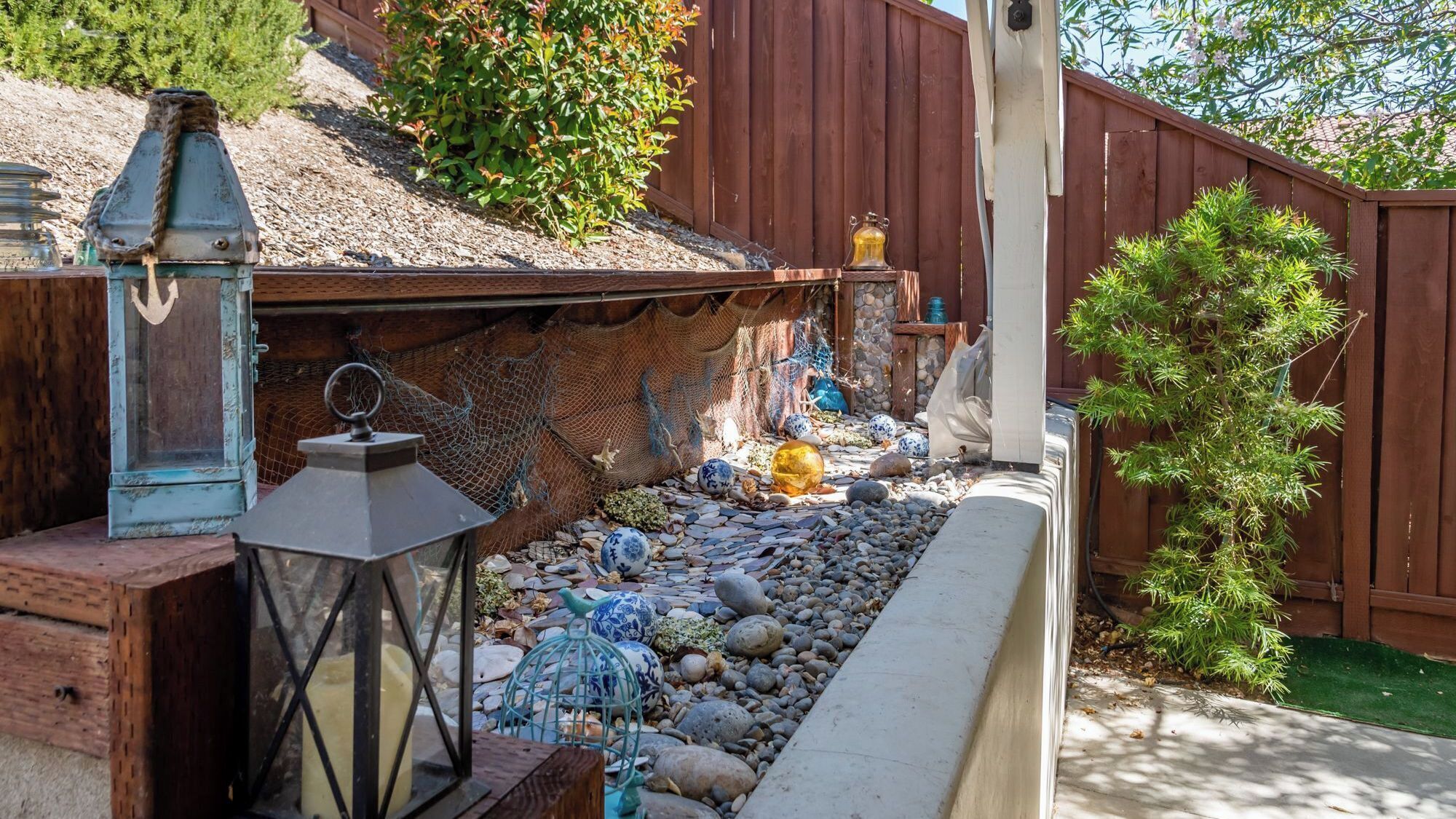 A garden with a wooden fence, decorative lanterns, and a variety of stones and shells.