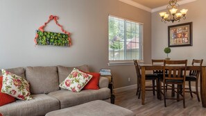 Ein Wohnzimmer mit einer Couch, einem Esstisch mit Stühlen, einer Deckenleuchte und einem Fenster mit Jalousien.