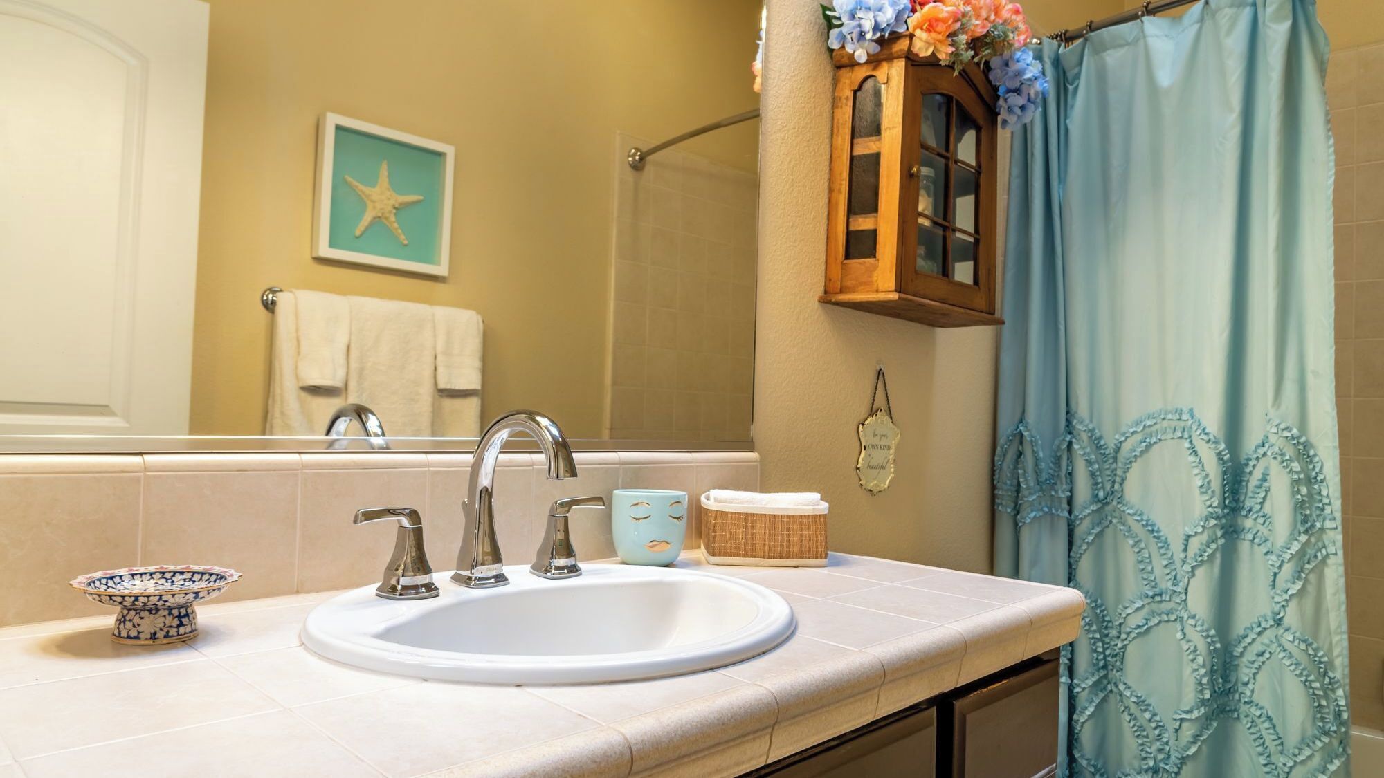 A bathroom with a sink, two faucets, a mirror, a towel rack, a starfish decoration, a cabinet, and a shower curtain.