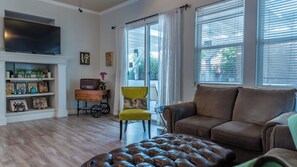 Ein Wohnzimmer mit Sofa, Hocker, Fernseher und einem kleinen Tisch mit Dekoration.