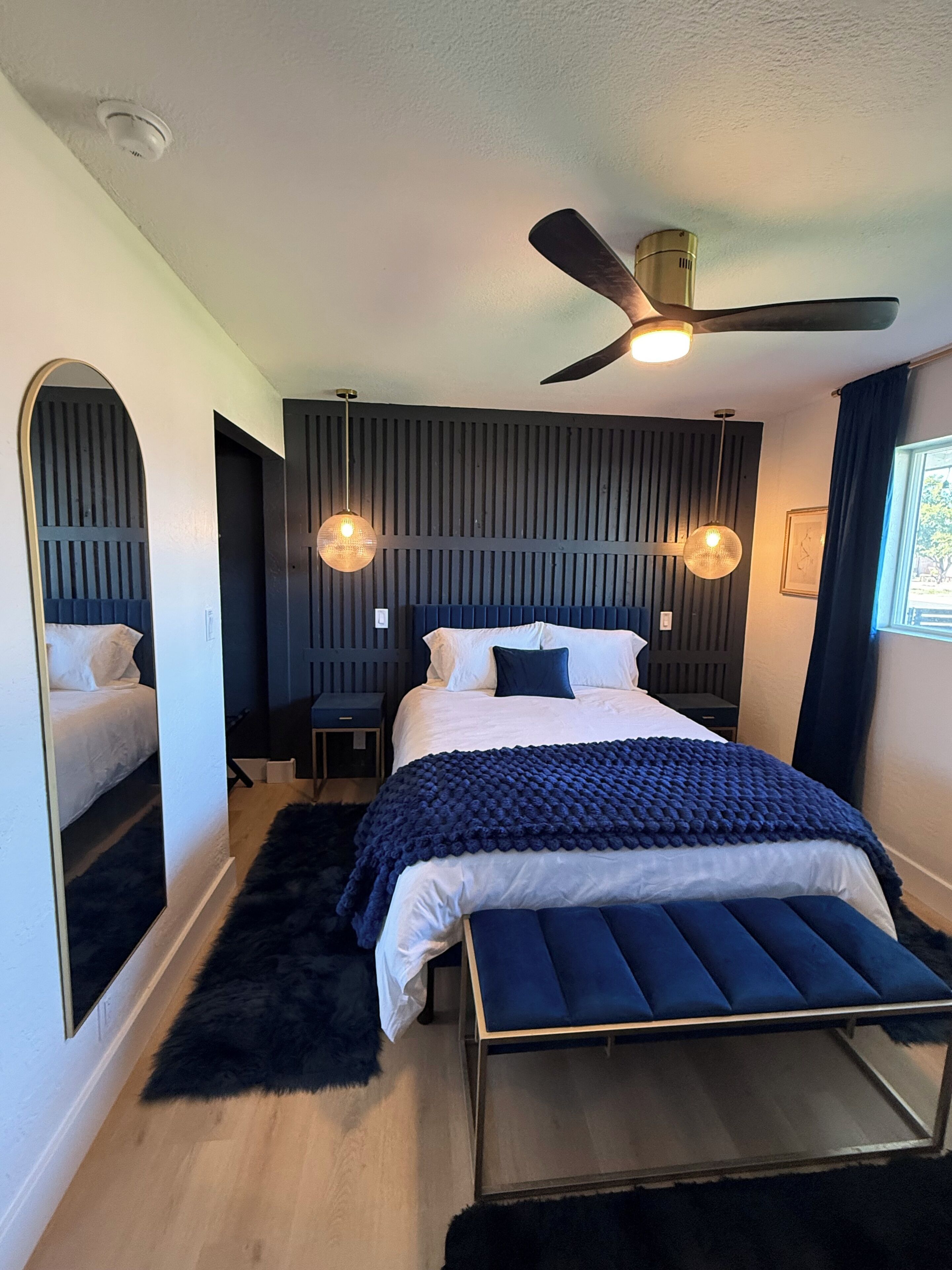 A modern bedroom with a bed, bench, ceiling fan, and wall-mounted lights.