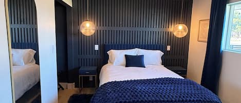 A modern bedroom with a bed, bench, ceiling fan, and wall-mounted lights.