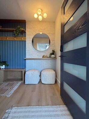 A hallway with a wooden floor, a blue wall, a round mirror, and two ottomans. - Updated Home! Minutes to Old Town&ASU Heated Pool Hot Tub Game Room Mini Golf! (Tempe)