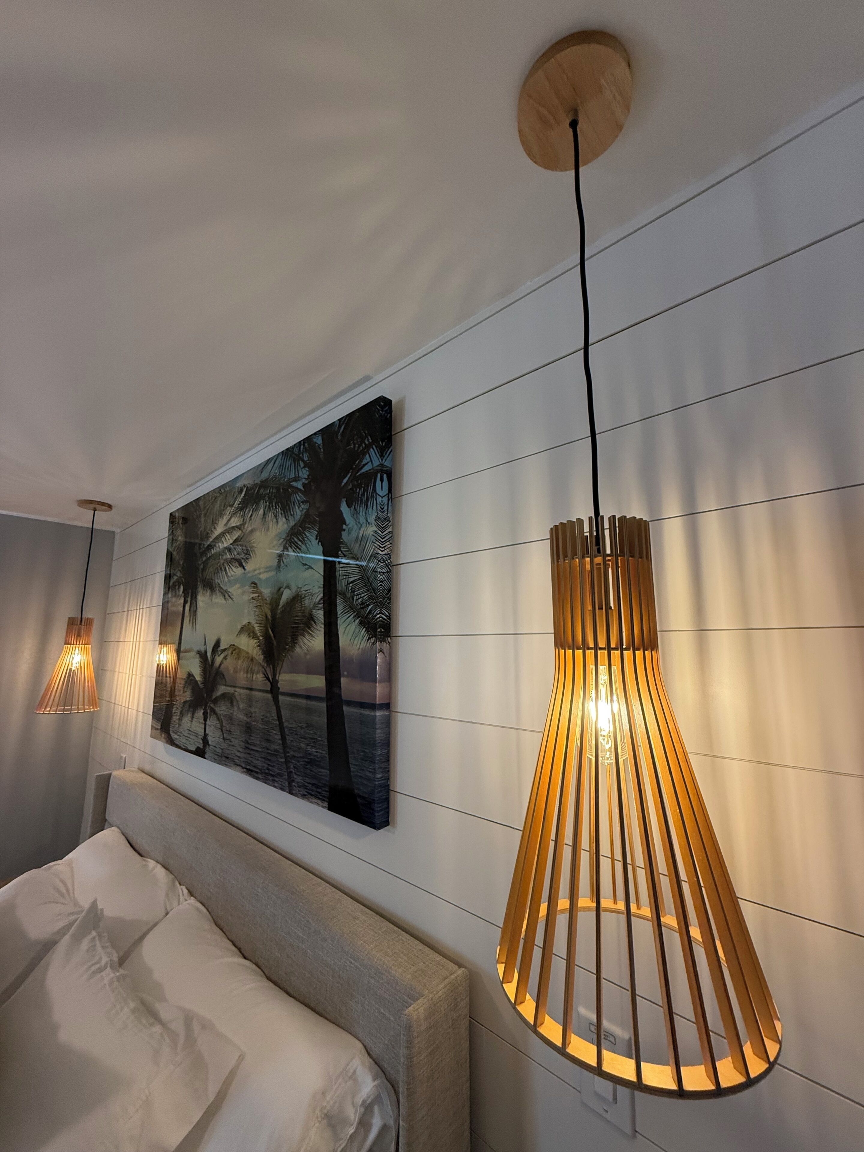 A bedroom with a bed, a wall-mounted painting, and a pendant light fixture.