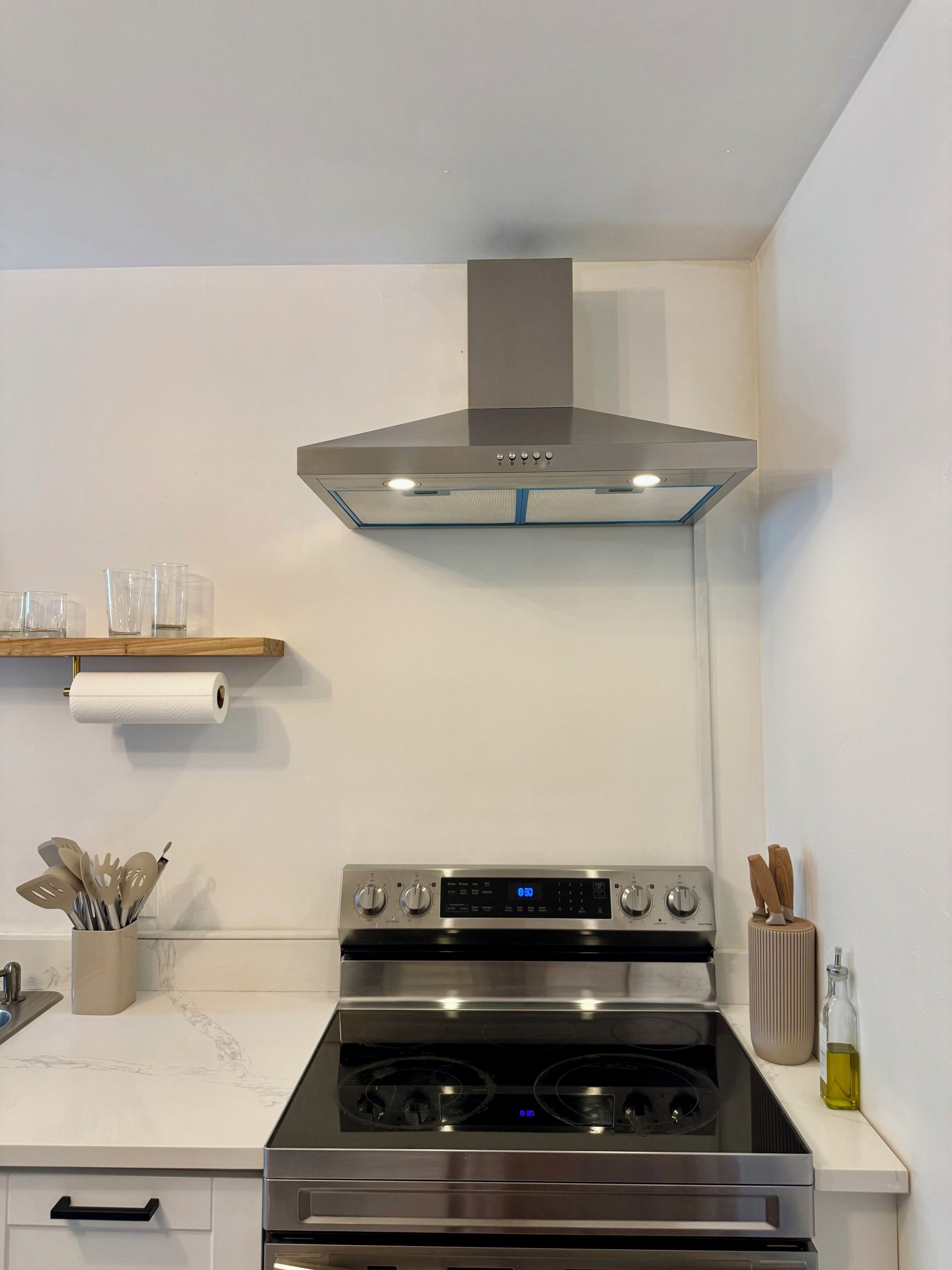 A modern kitchen with a stainless steel range hood, a built-in oven, and a marble countertop.