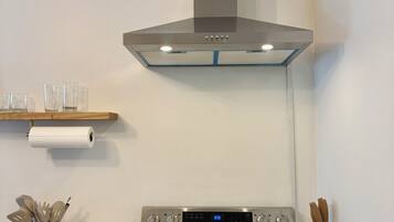 A modern kitchen with a stainless steel range hood, a built-in oven, and a marble countertop.