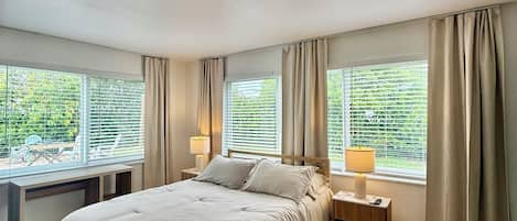Une chambre moderne avec un grand lit, deux tables de chevet et une vue sur la verdure.