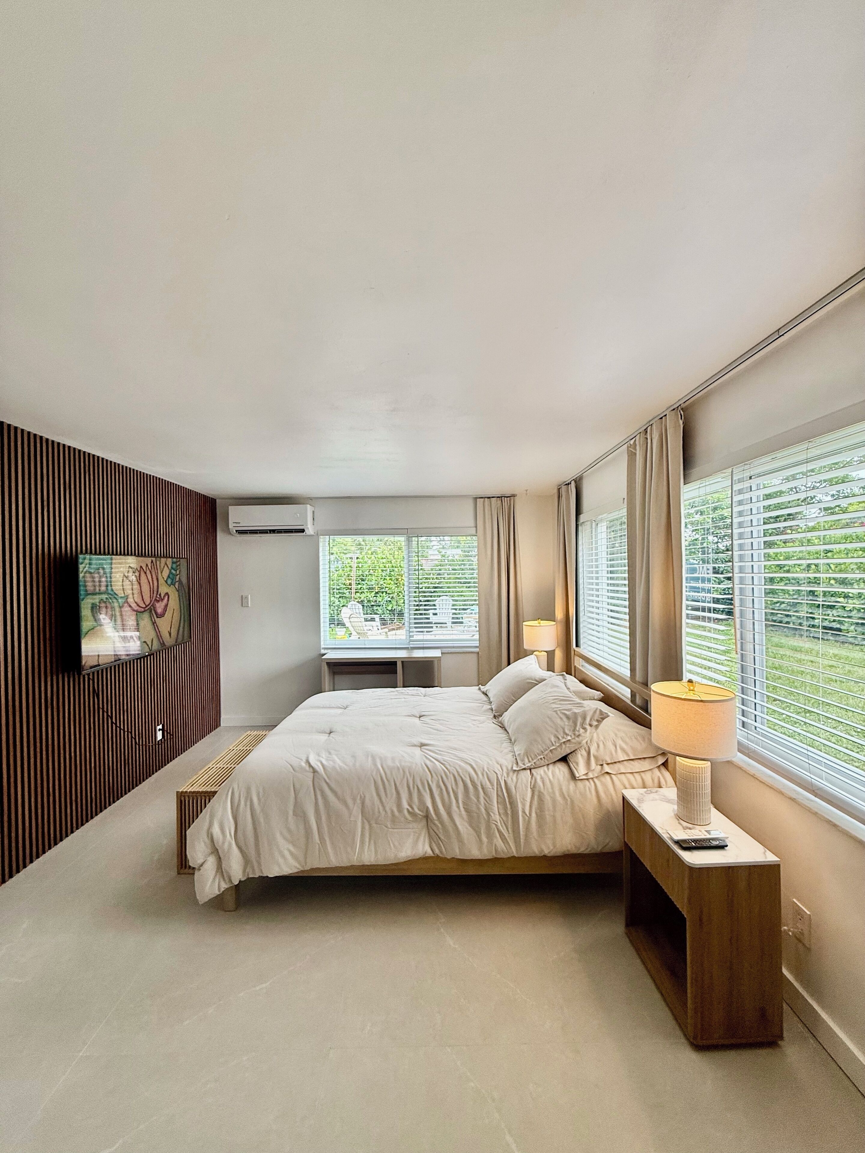 Un dormitorio moderno con cama, mesita de noche, lámpara y televisor montado en la pared.