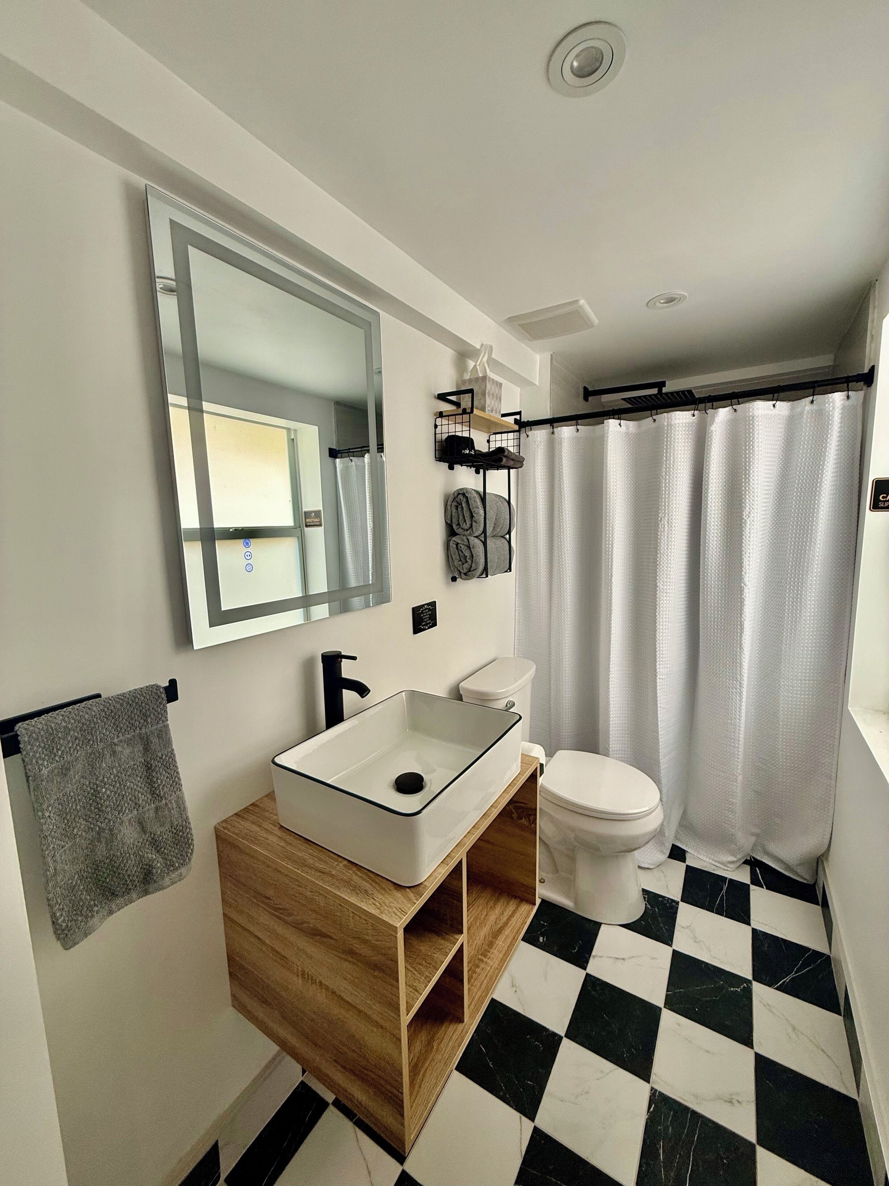 A bathroom with a white sink, wooden vanity, a toilet, and a shower curtain.