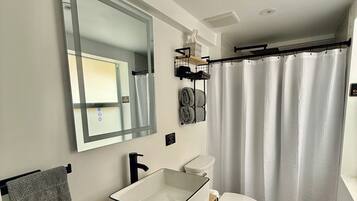 A bathroom with a white sink, wooden vanity, a toilet, and a shower curtain.
