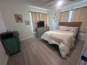 Um quarto com cama, cômoda, televisão e um armário verde.