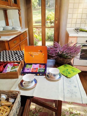 A kitchen with a table set for tea, a box of tea selection, and a window with a garden view.