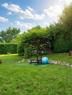 A well-maintained outdoor area with a weightlifting station, exercise ball, and a neatly trimmed hedge.
