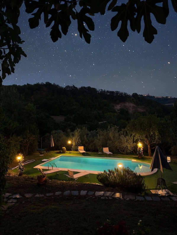 A swimming pool surrounded by lawn chairs and a tent, with a starry night sky above.