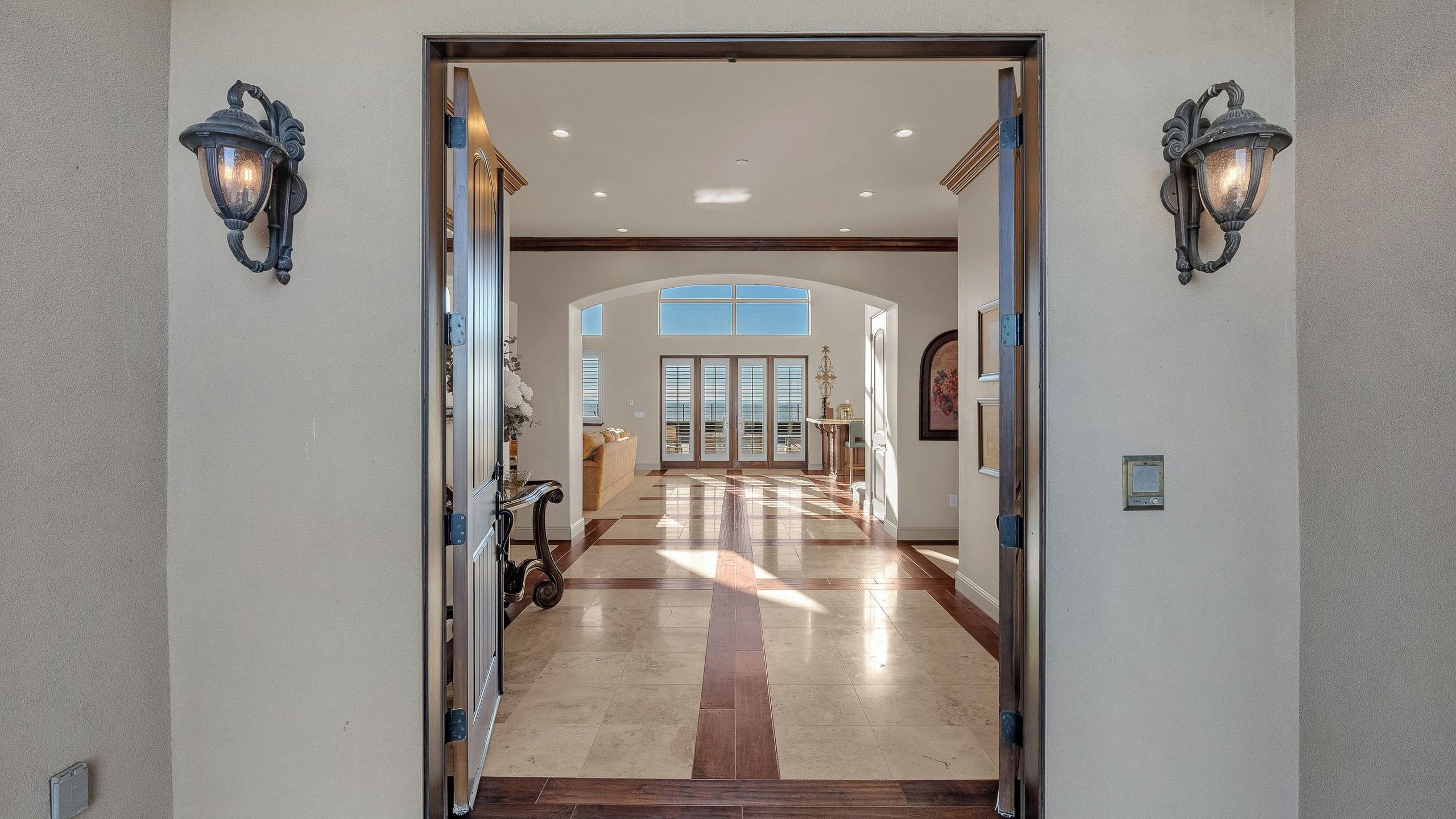Un pasillo espacioso con techo alto, vistas al cielo a través de amplias ventanas y una puerta que da a otra habitación.