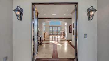 Un pasillo espacioso con techo alto, vistas al cielo a través de amplias ventanas y una puerta que da a otra habitación.