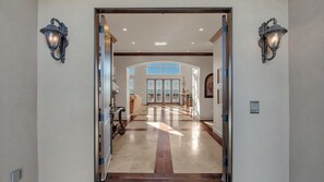 A spacious hallway with a high ceiling, a view of the sky through large windows, and a door leading to another room.