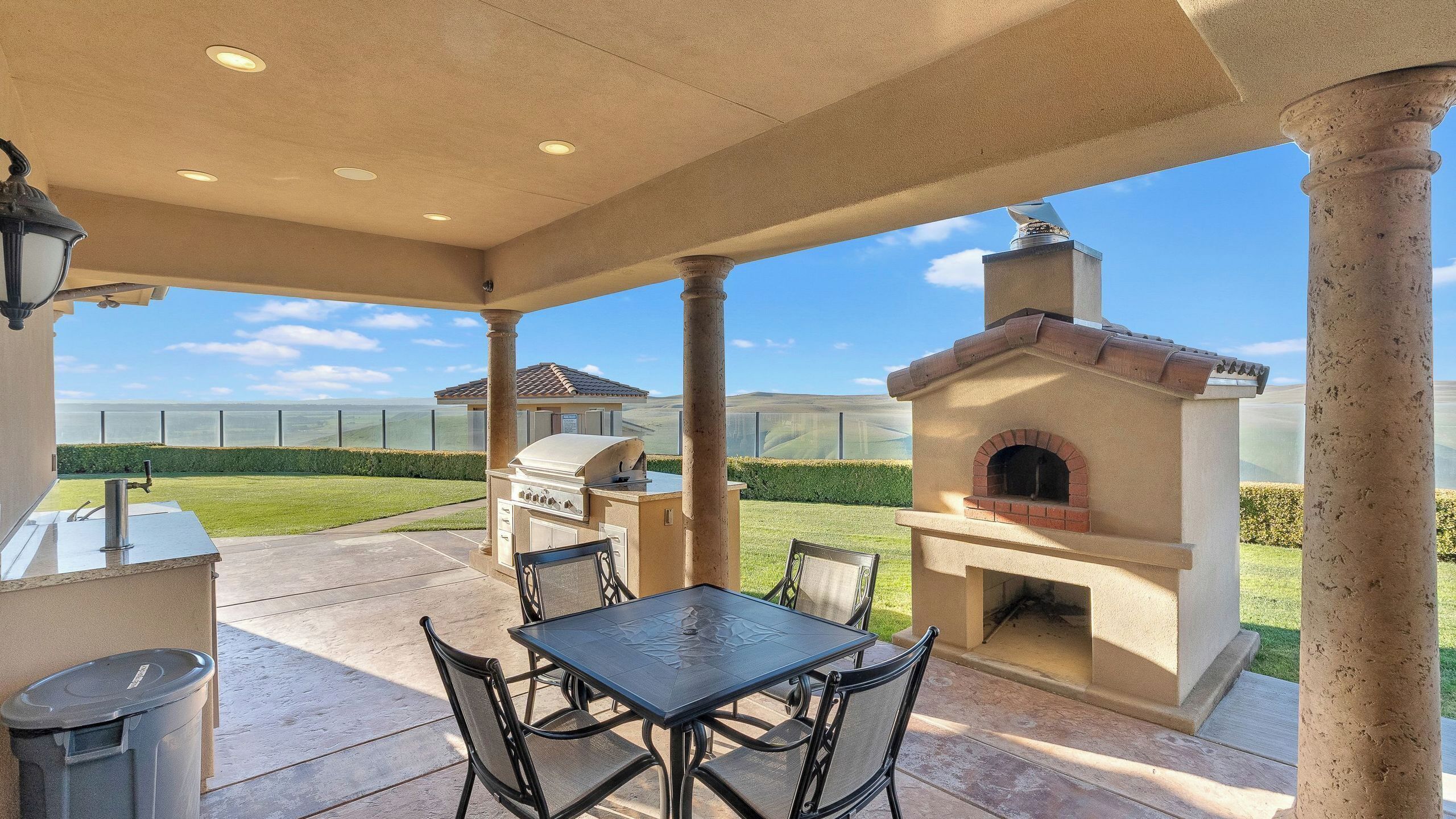 An outdoor patio with a grill, seating, and a brick oven.