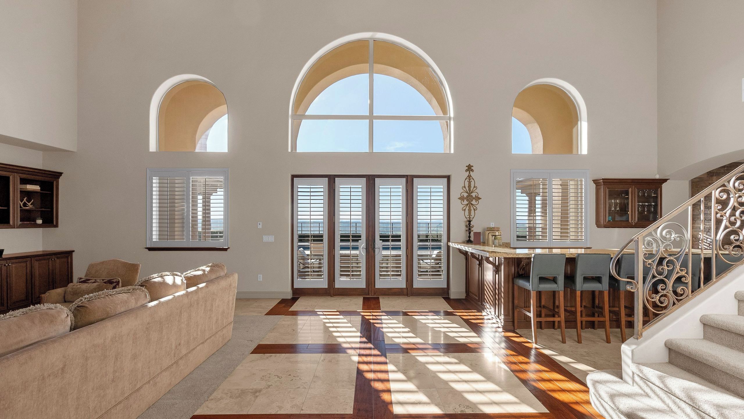 A spacious living room with a large sofa, a dining area with bar stools, and a staircase.