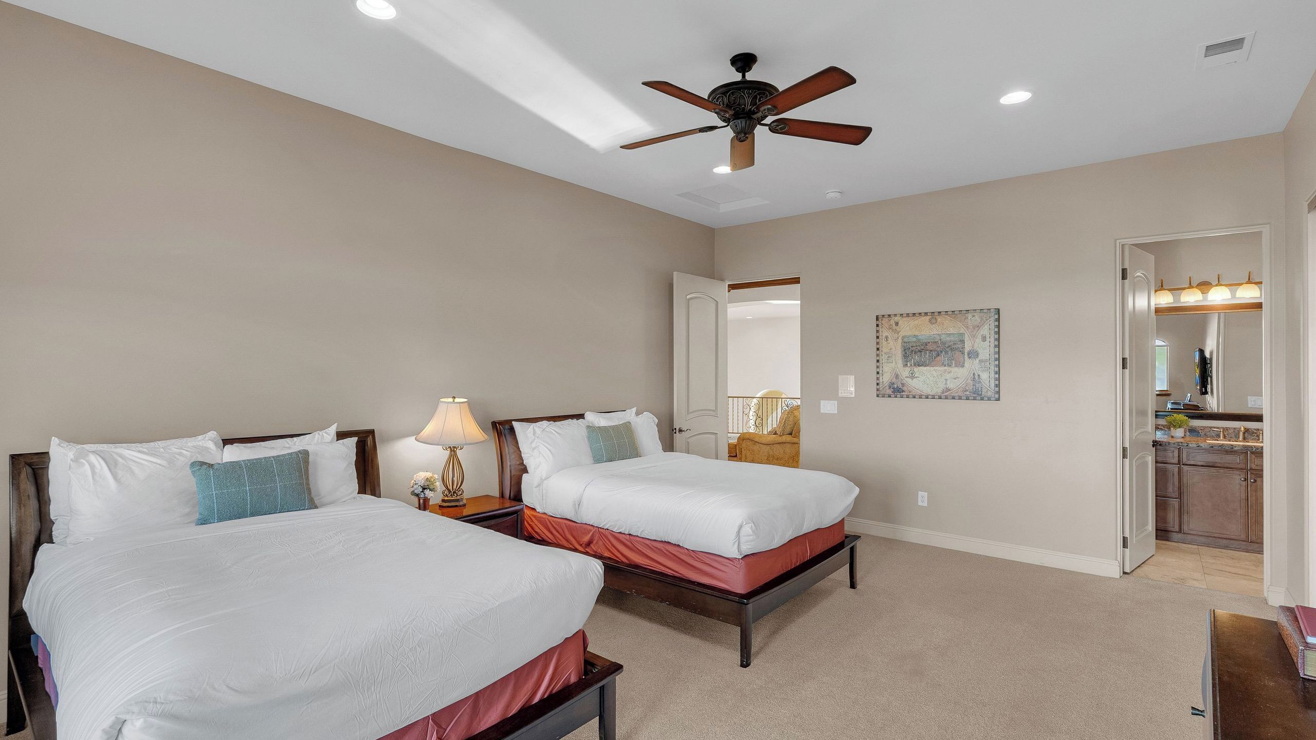 A bedroom with two beds, a ceiling fan, and a bathroom visible through an open door.