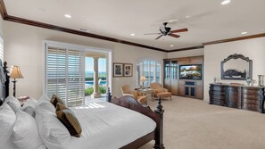 A bedroom with a large bed, a ceiling fan, and a view of the outdoors.