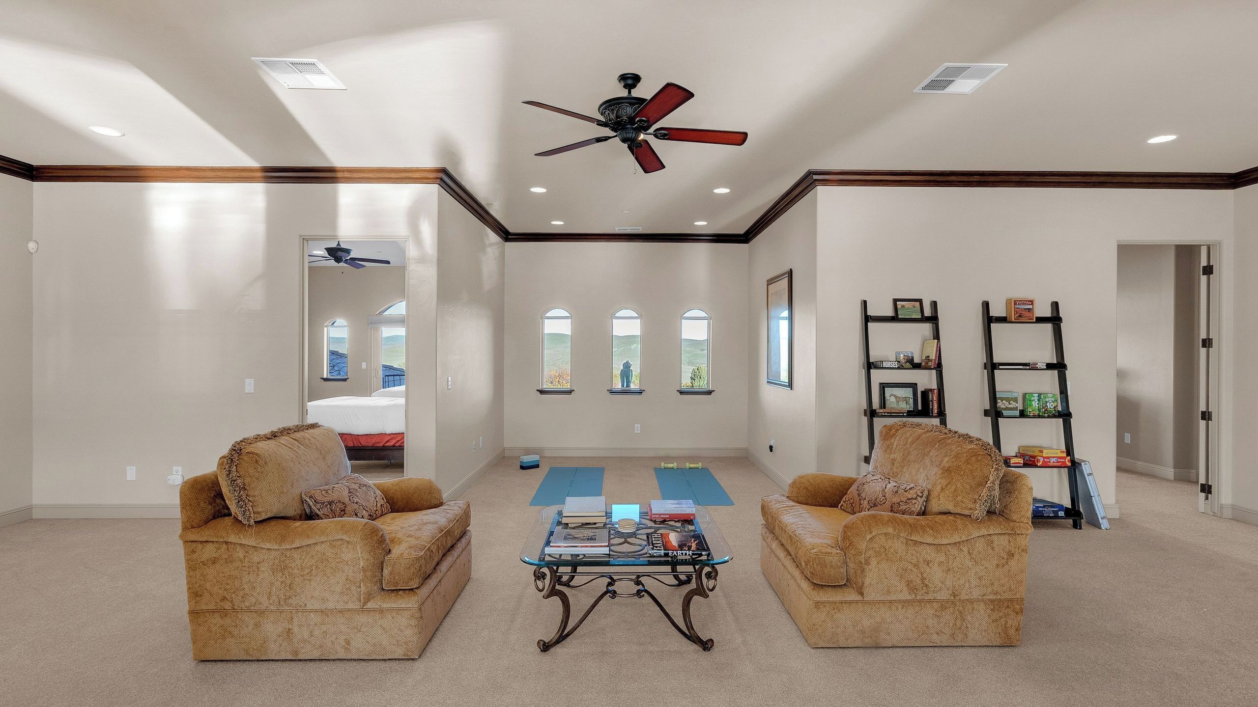 A spacious living room with two sofas facing a coffee table, a ceiling fan, and a view through large windows.