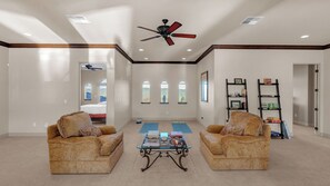 A spacious living room with two sofas facing a coffee table, a ceiling fan, and a view through large windows.