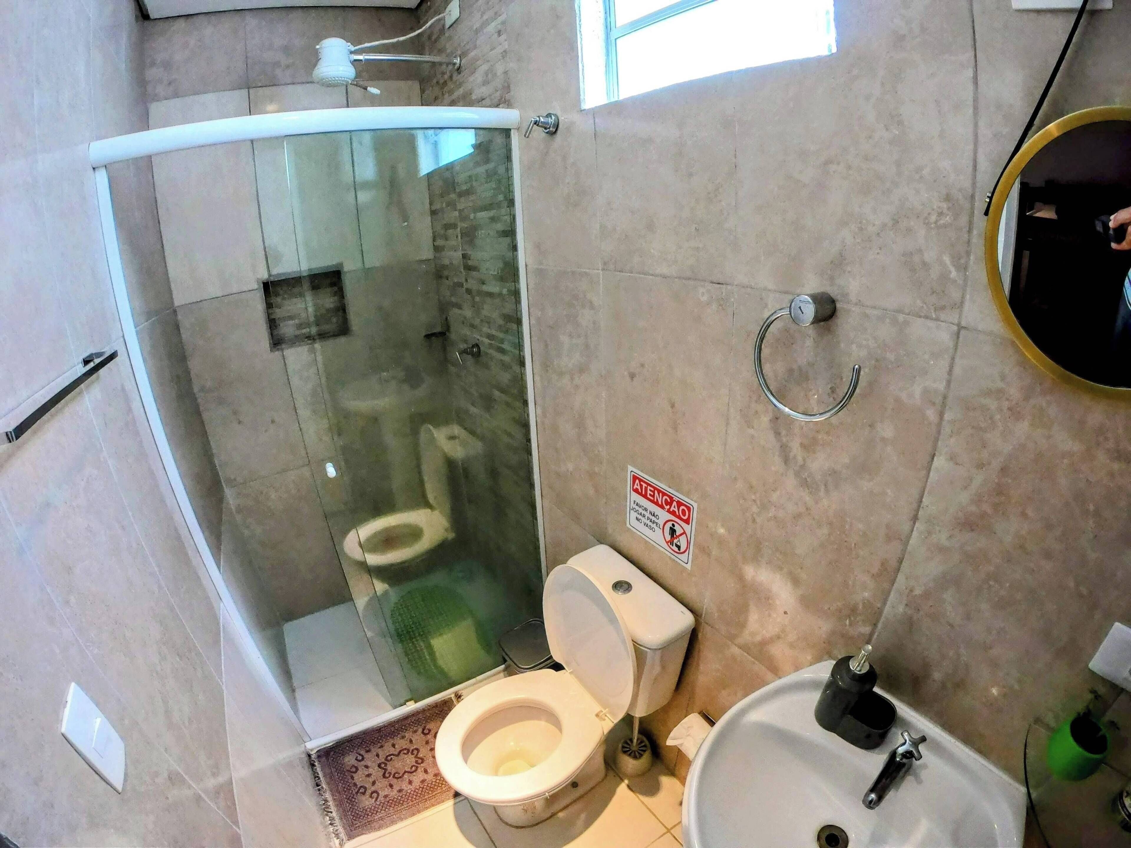 Casa de banho com chuveiro envidraçado, sanita e lavatório.
