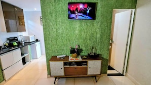 A modern kitchen with a flat-screen TV mounted on a green textured wall, a wooden cabinet with drawers, and a white door.