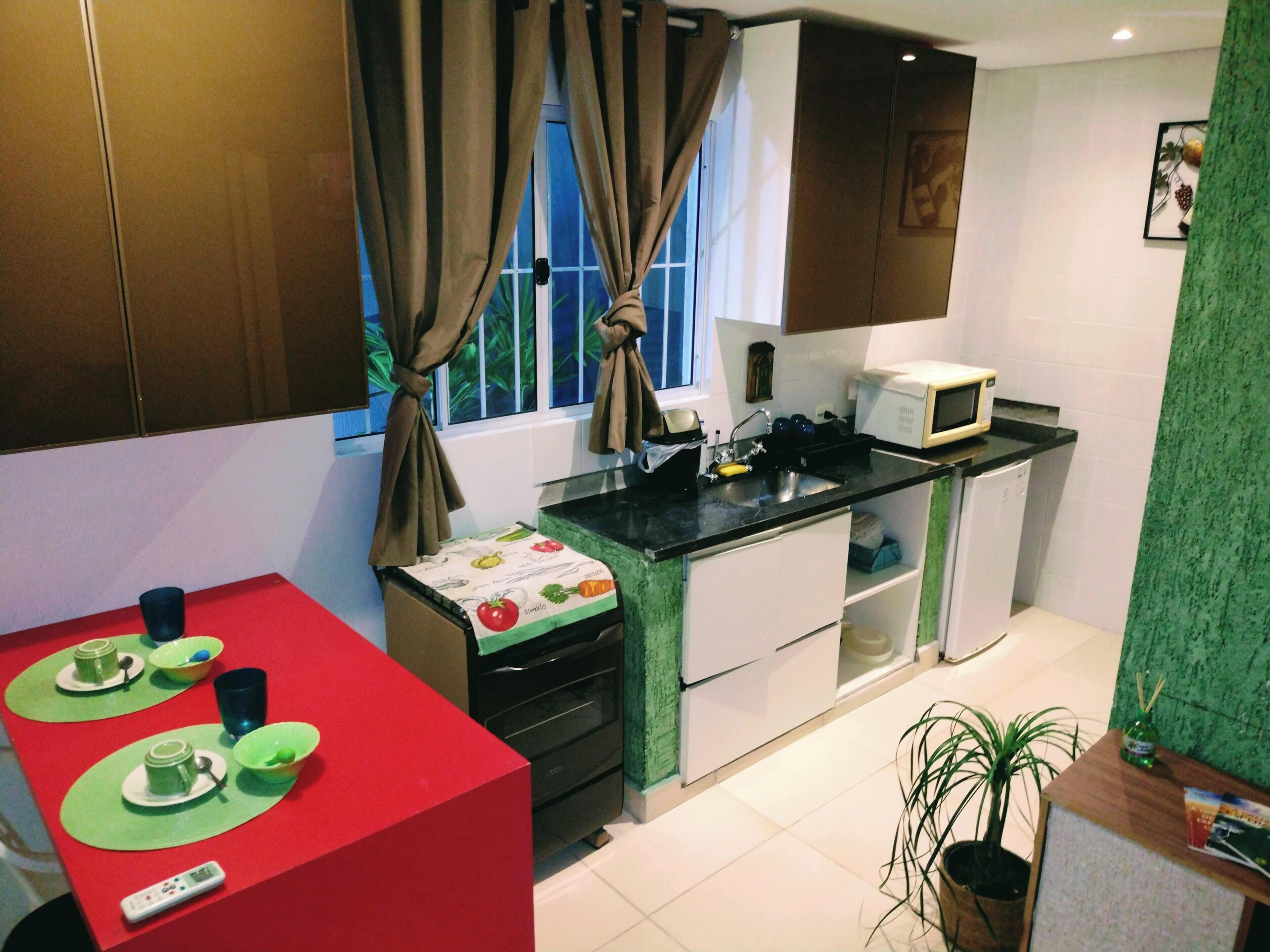 A compact kitchen with a microwave, sink, and a small dining area with a red table and green placemats.
