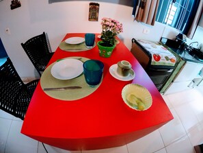 A dining area with a red table, plates, cutlery, and a potted plant.