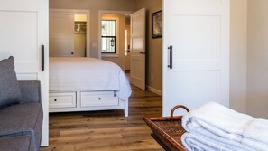 Quarto com cama, cadeira, mesa de cabeceira e porta que dá para outro aposento.