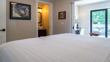 Un dormitorio con una cama grande, un baño con lavamanos y espejo, y vista al exterior por una puerta corredera.