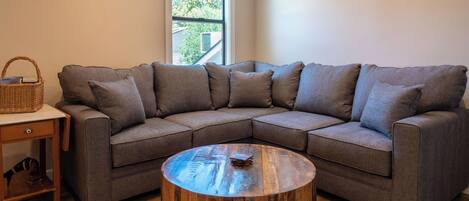 A modern living room with a sectional sofa, a wooden coffee table, and a small side table with a basket.